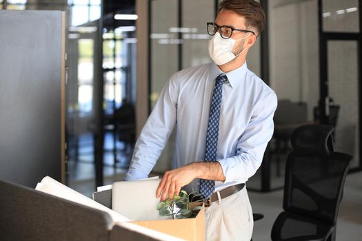 Dismissal employee in an epidemic coronavirus. Sad dismissed worker are taking his office supplies with him from office.