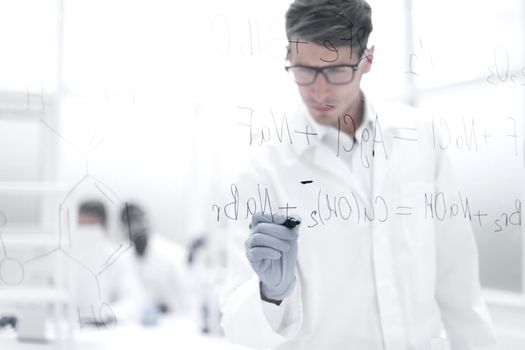 serious scientist writes a chemical formula on a glass Board.