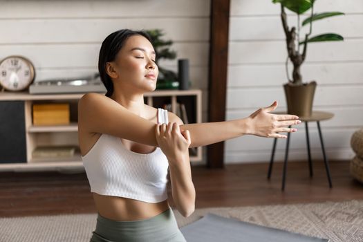 Smiling asian woman doing stretches, fitness workout at home in living room, wearing sport clothing.