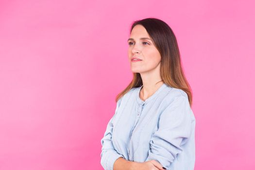 Portrait of a beautiful woman with long brown hair wearing blue cotton blouse, standing waist up on a pink background with copyspace