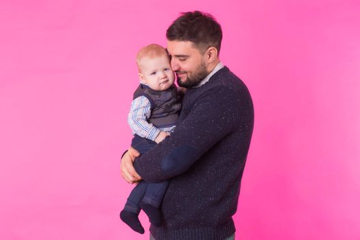 Happy father holding baby son in hands over pink background