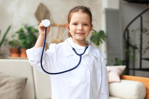 Smiling little girl in medical uniform playing with stethoscope at home.