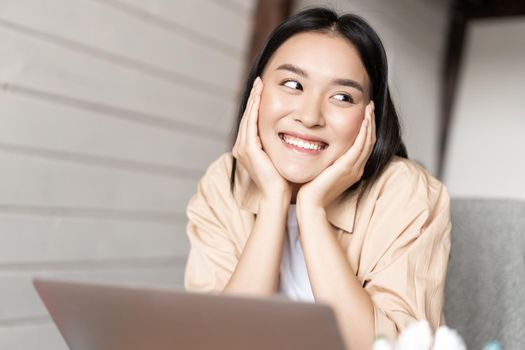 Asian woman smiling while resting, using laptop, watching videos or surfing net on computer, working from home