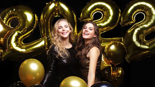 Happy gorgeous girls in stylish sexy party dresses holding gold 2022 balloons, having fun at Christmas or New Year's Eve Party.