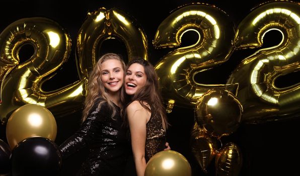 Happy gorgeous girls in stylish sexy party dresses holding gold 2022 balloons, having fun at Christmas or New Year's Eve Party.