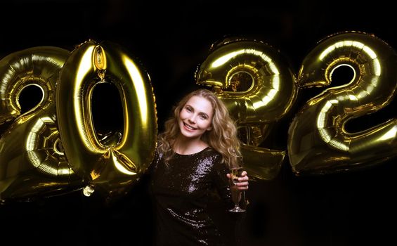 Happy gorgeous girl in stylish sexy party dress holding gold 2022 balloons, having fun at Christmas or New Year's Eve Party.