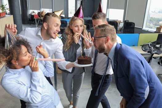 Happy business team with birthday cake are greeting colleague at office party