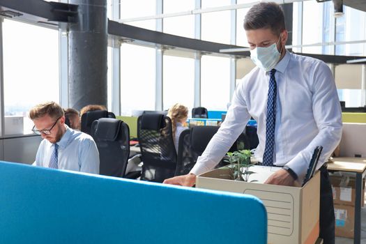 Dismissal employee in preventive medical mask in an epidemic coronavirus. Sad dismissed worker are taking his office supplies with him from office.