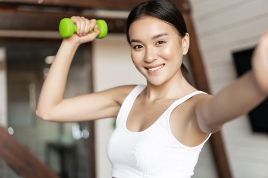Smiling korean girl taking selfie with dumbbell, workout at home during pandemic, wearing activewear
