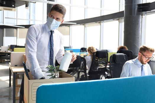 Dismissal employee in preventive medical mask in an epidemic coronavirus. Sad dismissed worker are taking his office supplies with him from office.