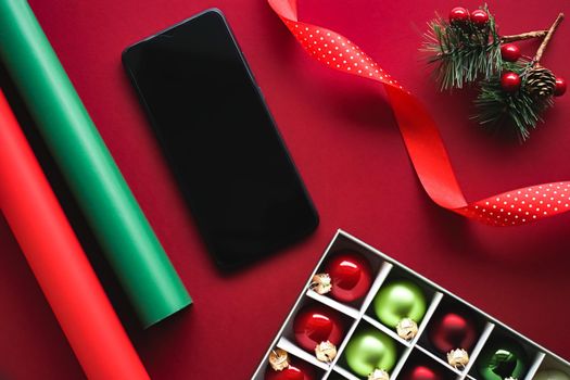 Christmas phone app and holiday message concept. Smartphone with blank black screen and xmas decoration on red background as flat lay mockup design