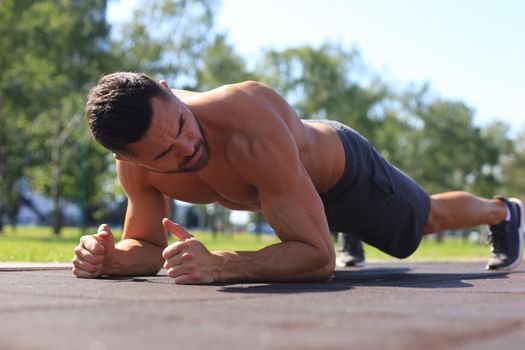 Focused muscular guy doing plank exercise outdoors