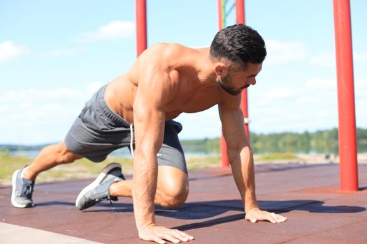Focused muscular guy doing plank exercise outdoors