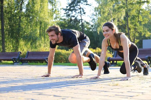 Young couple doing exercise together while working out outdoors in park.