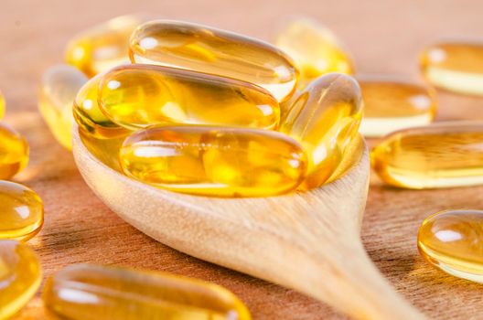 Cod liver oil omega 3 gel capsules on a spoon on wooden background.