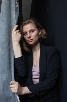 caucasian woman with short hair posing in black suit jacket, holding curtain