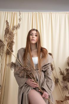 pretty woman in beige raincoat on pastel fabric background. fashion photo shoot