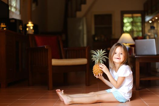 Little nice girl sitting on floor and playing with pineapple.
