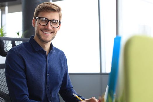 Good looking young business man looking at camera and smiling while sitting in the office.