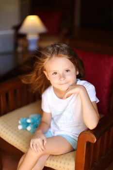 Little pretty female model sitting with toy in wooden chair.