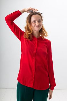 young caucasian redheaded girl in red shirt fooling around with mobile phone