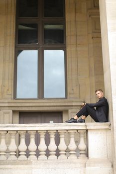 Young handsome boy sitting on balcony concrete banister in Paris.