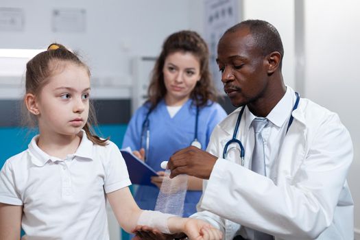 African american pediatrician doctor bandage fractured arm of girl patient