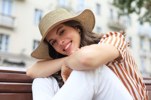 Beautiful smiling young brunette woman sitting on bench in park.