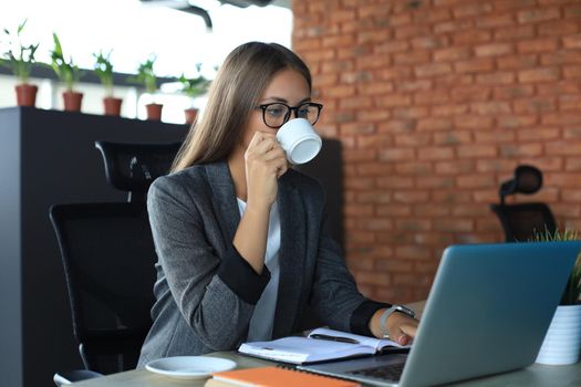 Beautiful business woman is holding coffee cup and smiling while sitting at her working place