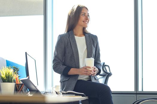 Attractive business woman is holding hot drink while sitting in the office.
