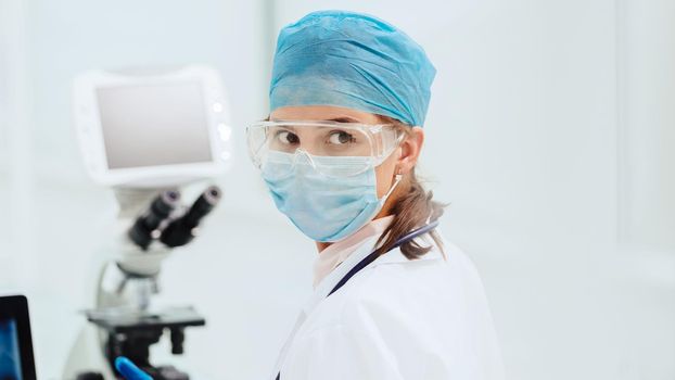 female microbiologist in a protective mask looking at you.