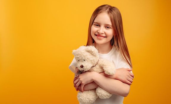 Girl with teddy bear isolated on yellow background