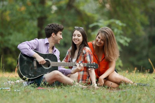 group of students with a guitar relax sitting on the grass in the city Park