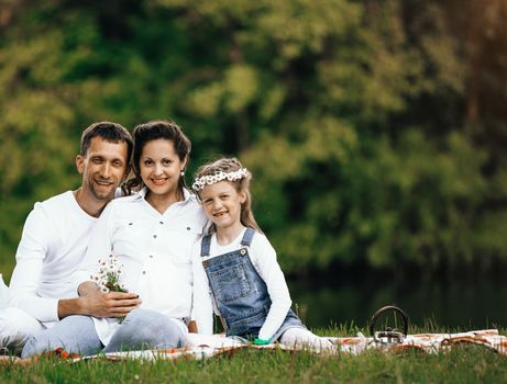 pregnant mother and happy father and little daughter at a picnic in the Park on a Sunny day. the photo has a empty space for your text