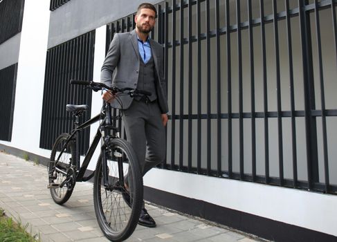 Confident young businessman walking with bicycle on the street in town.