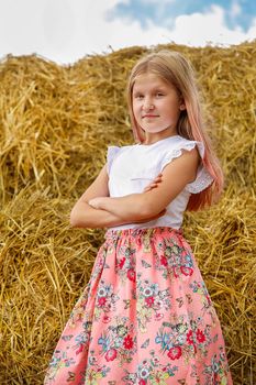 A blonde schoolgirl in a pink dress climbed on large bales of straw on a hot summer day