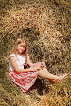 Cute girl with long hair sitting on a bale of straw in summer