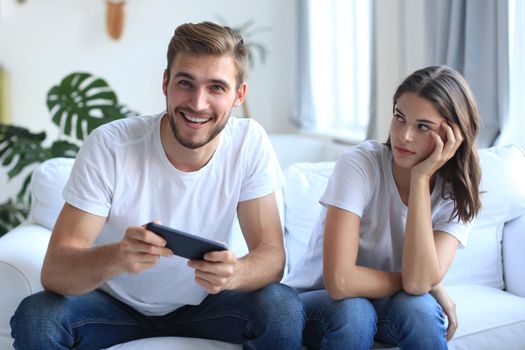 Man playing video games while his girlfriend is getting mad at him in their living room.