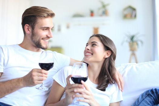 Young loving couple drinking a glass of red wine in their living room.