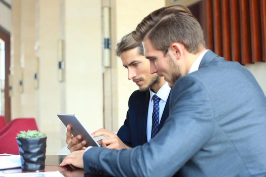Two young businessmen using touchpad at meeting.