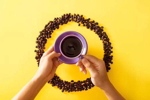 Hand holding cup of coffee on the yellow background