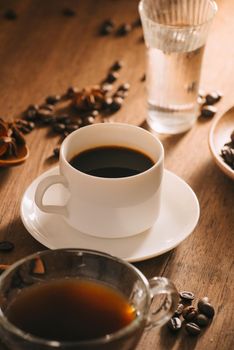 A cup of coffee with water, coffee beans and tea on wooden bakcground