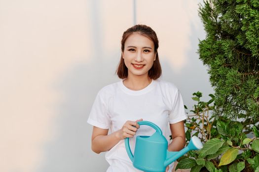 Young Asian woman holding watering can in white tshirt in her garden.