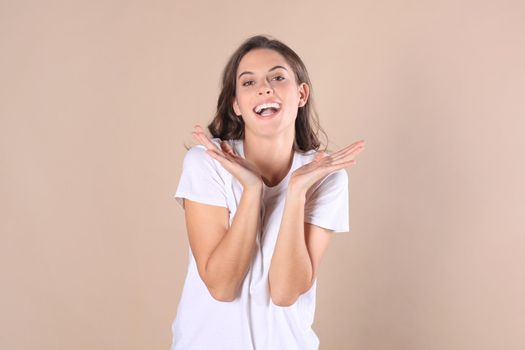 Young woman in casual clothing wondering and screaming isolated over beige background