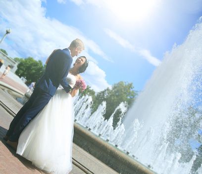 newlywed couple standing near a fountain .