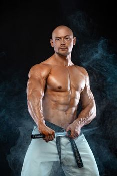 Karate fighter on black background with smoke. Shirtless man samurai with Japanese sword. Fit man sportsmen bodybuilder physique and athlete.