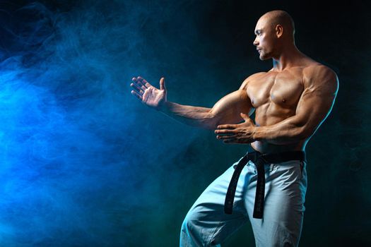 Karate or taekwondo fighter on black background with smoke. Fit man sportsmen bodybuilder physique and athlete. Men's sport motivation.