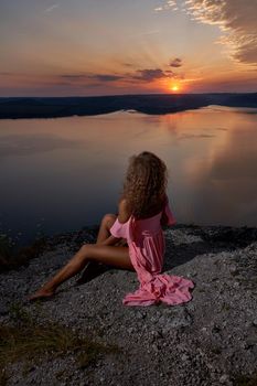 Sexy girl sitting and admiring sundown near lake.
