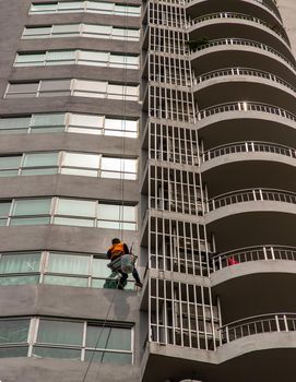 Unidentified worker use ropes outside the building cleaning the windows service on high-rise condominium building. 