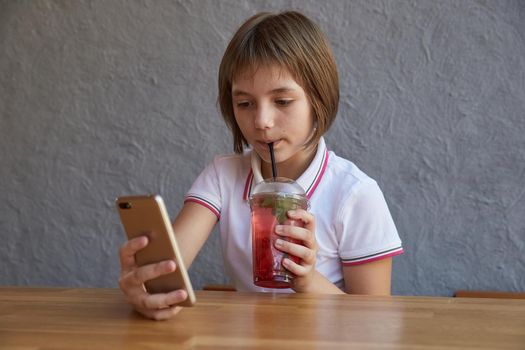 girl reading information on phone, drinking red icy cocktail at table of cafe